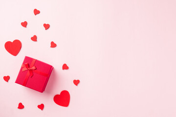 Valentines' day background. Red gift box with ribbon bow and wood red hearts shaped composition greeting card for love isolated on pink background with copy space. Top View from above