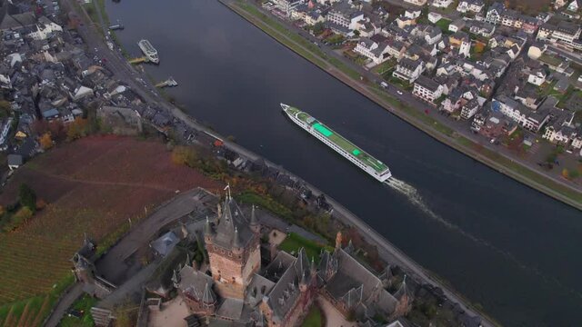 River cruise ship in Moselle passing by Reichsburg Cochem castle on hill, aerial