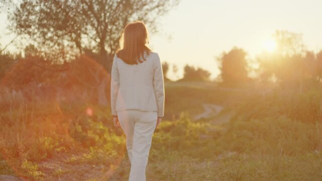 Ragazza con cappotto bianco cammina di spalle verso la natura