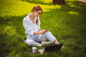 beautiful girl studies, works with laptop, blogger, makes notes, distance education outdoor in park 