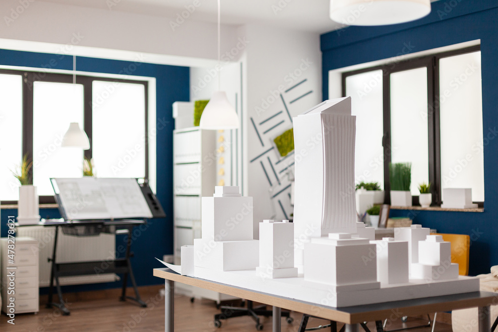 Poster table with white architectural scale foam model of building complex in empty modern architect office