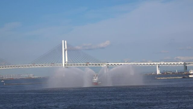 A tugboat used a water jet to send off "Akira II" with a spectacular water jet. Yokohama Bay is in the background. The "Akira II" departure. YOKOHAMA, JAPAN - June 3, 2019.