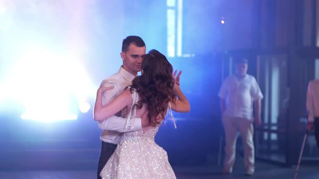 the first wedding dance of the newlyweds against a background of thick white smoke with flashing colorful lights. the bride and groom tenderly embrace in a dance against the background of the guests.