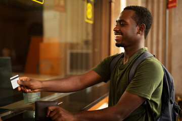 Young man buying a ticket for train with a credit card. Handsome smiling man going to a trip