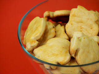 a variety of curd biscuits in the shape of fish, covered with orange-yellow jam, is in a round glass bowl on a red background, side view. homemade cakes
