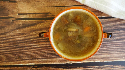 mushroom soup with Polish mushrooms, carrots, potatoes and onions in a brown plate stands on a wooden table next to a beige towel