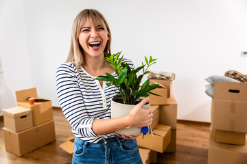 Portrait of young woman in apartment holding houseplant of her new home.