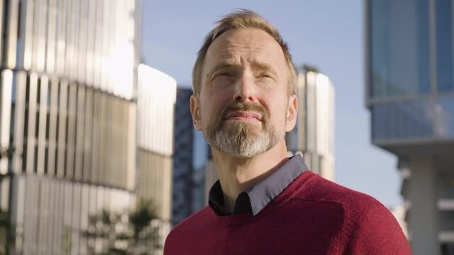 A middle-aged handsome Caucasian man looks around in an urban area - office buildings in the blurry background - closeup
