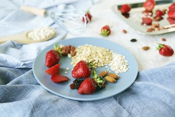 Healthy breakfast ingredients on the table, strawberries, oatmeal and nuts on a light background
