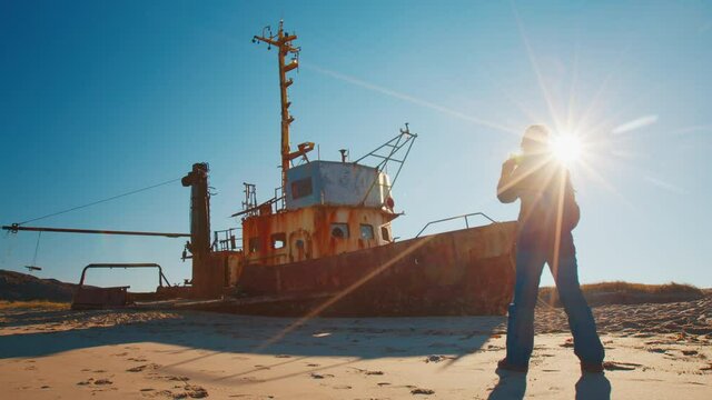 Tourist in Teriberka. Woman takes pictures with smartphone of the beached ship near the town of Teriberka in Russia during sunny day