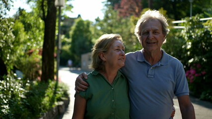 Two happy older people walking outside smiling, senior couple together in outdoor nature walk