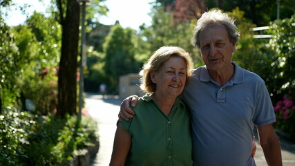 Obraz premium Two happy older people walking outside smiling, senior couple together in outdoor nature walk
