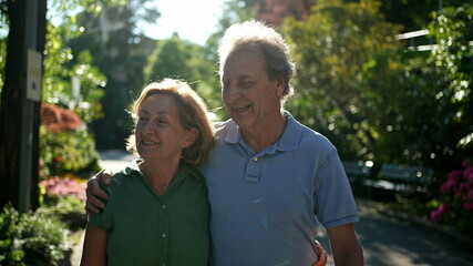 Two happy older people walking outside smiling, senior couple together in outdoor nature walk