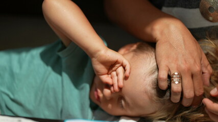 Tired child rubbing eye with hand, mother caressing hair