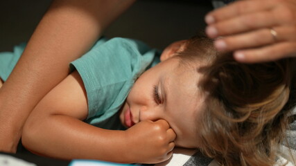 Sleepy child rubbing eye with hand, kid lying down resting