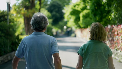 Naklejka premium Romantic senior husband putting arm around wife, back view of older couple walking together in green path
