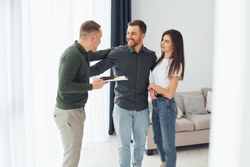 Salesman helps young couple in choosing an apartment. Conception of business and rent