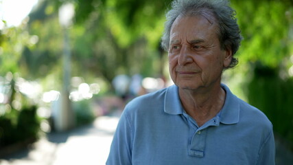 Pensive senior man walking outside in city green nature path
