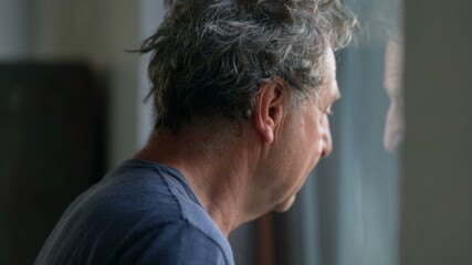 Pensive senior man standing by window looking outside. Thoughtful old person