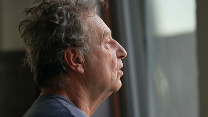 Obraz premium Pensive senior man standing by window looking outside. Thoughtful old person