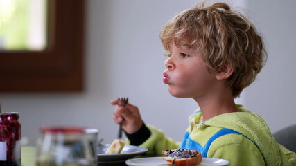 Pensive child sitting at breakfast table eating fruit. thoughtful boy