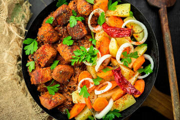 Stew with meat and vegetables in black iron dish. Traditional  gourmet goulash in a rustic kitchen. Top view