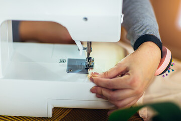 Woman sewing while sitting at her working place in fashion workshop. Close up
