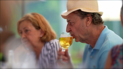 Older man drinking beer, candid senior drinks draft beer at restaurant