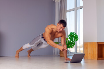 Fototapeta Online trainer. On-line sports. fitness and healthy lifestyle concept. Man with laptop computer doing plank exercise at home during a pandemic. obraz