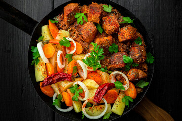 Stew with meat and vegetables in black iron dish. Traditional  gourmet goulash in a rustic kitchen. Top view