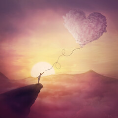 A person on the cliff and a heart shaped cloud like a kite raising up in the air. Magical scene,...