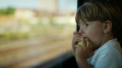 Little boy eating apple snack while riding train looking out window