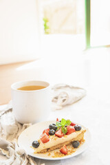 piece of strawberry and blueberry cheescake on plate and cup of tea served for breakfast at home, hotel or cafe. Dessert meal, sweet food . High quality photo