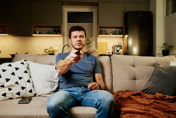 Obraz premium Man watching tv set at lazy weekend, resting at living room, use remote control to switch channels