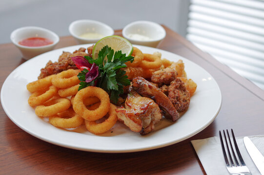 Deep Fried Snacks Calamari Rings Onion Ring Buffalo Wings Drumsticks Karaage Chicken Nuggets On White Round Plate With Sliced Lime And Dips 