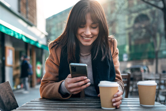 Pretty young woman using her mobile phone while drinking cup of coffee in the terrace of a coffee shop.
