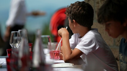 Children sitting at restaurant table, kid drinking from straw