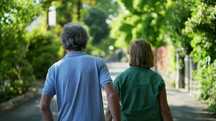 Naklejka premium Back of senior couple walking outside in green city Back of senior couple walking outside in green city
