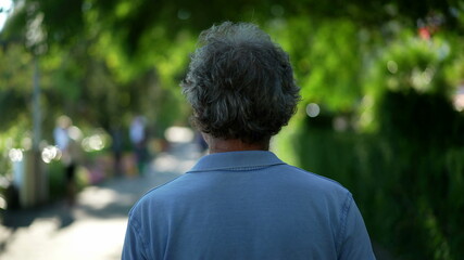 Back of person walking in nature, senior man in 60s in green path