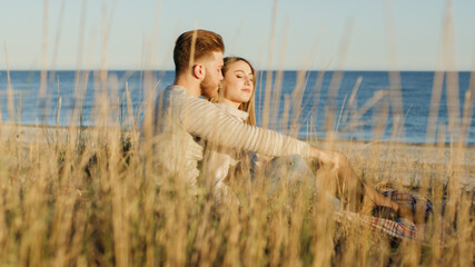 Coppia di ragazzo e ragazza si abbracciano seduti in spiaggia vicino all'oceano