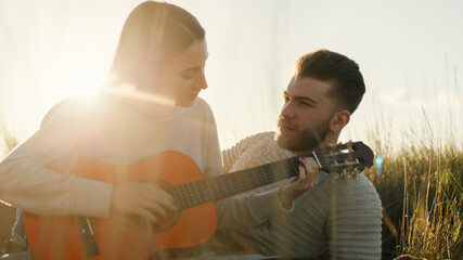 Coppia di ragazza e ragazzo suona la chitarra seduti sul parco al tramonto