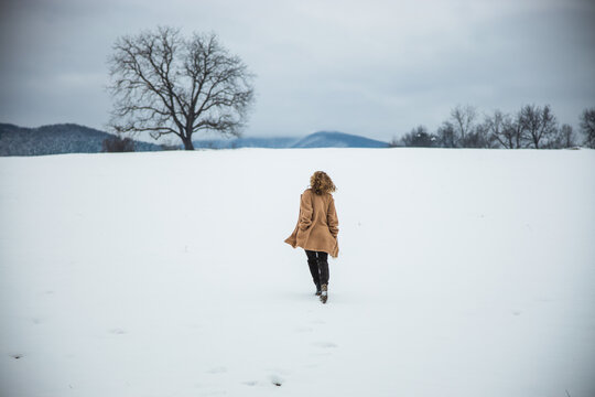 Woman in brown coat runs on a snow field. Mountains in the distance. Free spirit girl. Winter season. High quality photo