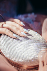 Girl with long nails holds a glittering white purse. Prom day. Girl has her first prom. High quality photo