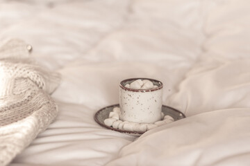 Morning coffee cup, Hot cocoa with marshmallow in a white ceramic mug , warm knitted sweater in bed on white blanket. Winter morning at home, special occasions,
