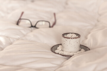 Fototapeta na wymiar Morning coffee cup, Hot cocoa with marshmallow in a white ceramic mug in bed on white blanket. Winter morning at home, special occasions, holidays,