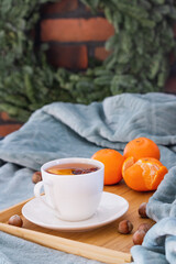Cup of hot tea served in bed. Tangerines and hazelnuts. Christmas wreath on brick wall.