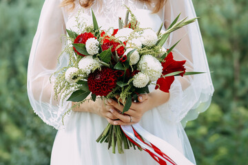 Wedding bouquet of fresh flowers in bride's hands, close-up. Young bride holding a bouquet of white and red flowers.