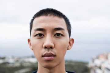 Young asian guy looking serious at camera outdoor - Focus on face