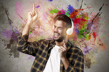 Handsome beard guy with headphones enjoying music and pointing fingers upwards on stained background, urban graffiti style.