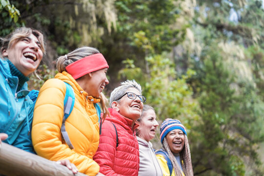 Multiracial women having fun exploring nature on trekking day in mountain forest - Focus on center senior face
